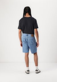 Lichtblauwe denim shorts met een relaxte pasvorm, voorzien van een tan leren label op de achterkant en twee achterzakken. Gecombineerd met een zwart T-shirt.