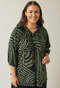 Blusa verde e nera con motivo, maniche a 3/4, collo tondo, bottoni e vestibilità ampia. Caratterizzata da disegni astratti con linee curve.