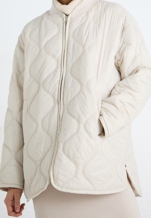 Beige gestepptes Jackett mit Wellenmuster, ausgestattet mit einem hohen Kragen, einem durchgehenden Reißverschluss und seitlichen Taschen. Weiches, leichtes Material mit einer glatten Textur.