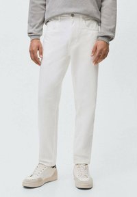 Jeans de mezclilla blanca con corte recto, que cuentan con bolsillos laterales y cierre de un solo botón, combinados con zapatillas casuales de color claro.