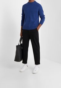 Niebieski dzianinowy sweter, czarne zwężane spodnie, białe tenisówki. W ręku trzyma czarną torbę typu tote. Gładka faktura, prążkowane mankiety i dół. Minimalistyczny fason.