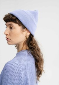 Brede gebreide muts in lichtblauw, met een ribbelpatroon en een puntige top. Gecombineerd met een bijpassende gebreide trui met een gestructureerd patroon.