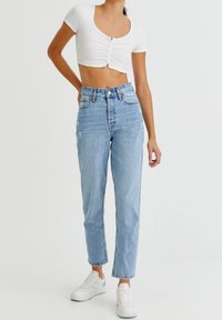 Top court blanc à côtes avec des manches courtes, associé à un jean taille haute bleu clair avec des accents déchirés et des ourlets. Des baskets blanches complètent le look.