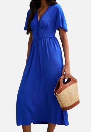 Femme portant une robe midi bleu à manches courtes avec un décolleté en V, tenant un sac seau tressé couleur camel avec des anses en cuir marron.