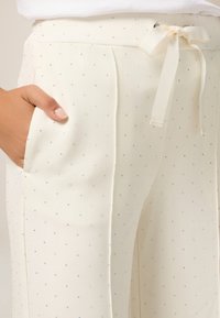 Pantalons blancs en tissu doux, ornés de petites étoiles argentées, avec une taille réglable par cordon et des poches latérales pour plus de praticité.