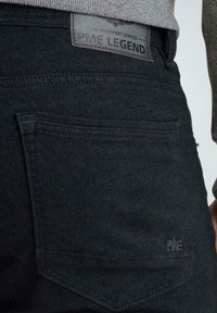 Vaqueros de mezclilla negra, con un sutil patrón de espiga, un bolsillo trasero rectangular y una etiqueta estampada con "PME Legend."