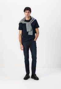 Mornarska majica, sivi pulover oko ramena, tamnoplave traperice i crne cipele. Elegantna izrada s ležernim izgledom.