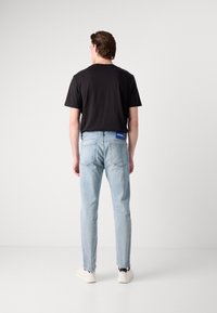Jeans de color azul claro con corte recto, combinados con una camiseta negra de manga corta. Etiqueta de Hugo notable en la parte trasera de la cintura. Zapatillas blancas.