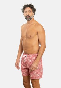 Bañador rojo con estampado que presenta un diseño floral blanco, cintura con cordón y un ajuste relajado, fabricado en un material ligero y de secado rápido.