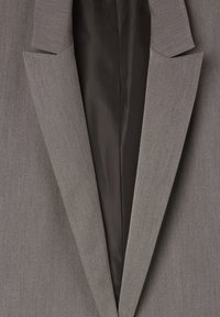Szary, dopasowany blazer o gładkiej fakturze, z klapami w stylu wyciętym i czarną satynową podszewką. Posiada jednorzędowy fason i ostre krawędzie.
