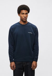 Tmavomodrá mikina vyrobená z hladkej tkaniny, s okrúhlym výstrihom, dlhými rukávmi a malým bielym logom na hrudi.