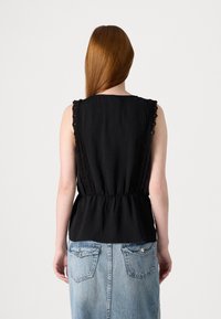 Svart ermeløs topp med blonde detaljer langs skuldrene, samlet midje, og en glatt tekstur, sammen med et blått denimskjørt med baklommer.