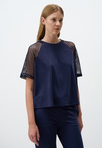 Top blu navy a maniche corte con corpo liscio e rete a maglie sulle maniche. Vestibilità comoda con scollatura tonda e dettagli testurizzati.
