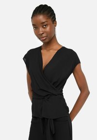 Top nero avvolgente con maniche corte, scollo a V, dettaglio con fiocco in vita, tessuto morbido, texture liscia e vestibilità slim.