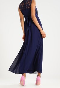 Navy long dress with a lace bodice, flowing chiffon skirt, and a tied waist detail, paired with pink high heels. Smooth texture throughout.
