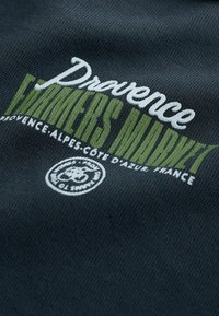 Mørkegrå stof med broderet tekst i hvid og grøn, der siger "Provence Farmers Market" med et cirkulært logo forneden.