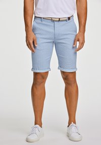 Ljusblå shorts i vävt tyg, med rak passform, uppvikta fållar och ett subtilt mönster. Kombinerat med vita sneakers.