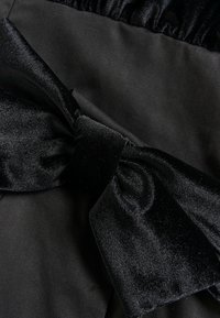 Tissu satin noir avec une texture lisse, présentant un grand nœud noué en matériau doux et brillant. Section froissée visible.