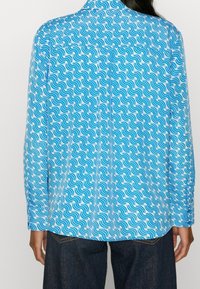 Camicia a maniche lunghe in tessuto azzurro chiaro con un motivo ondulato bianco e blu scuro, con colletto classico e polsini abbottonati.