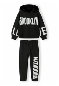 Svart träningsset innehåller en huva sweatshirt och matchande mjukisbyxor. Har djärv vit text: "BROOKLYN" och "LOVE." Mjuk struktur, avslappnad passform.