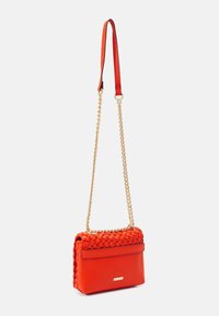 Červená kožená crossbody taška se tkaným vrchem, zlatým řetězem, hladkým povrchem a kovovým detailem na přední straně.