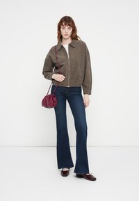 Olijfgroene bomberjack met elastische manchetten, gecombineerd met donkere flared jeans. Een bordeaux handtas en bijpassende schoenen maken de look compleet.