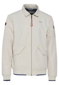 Light beige jacket with a collar, front zipper, two side pockets, and an additional zippered pocket on the sleeve. Ribbed hem and cuffs.