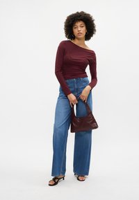 Burgundijas garām piedurknēm topi ar ziedu rotājumiem, saskaņots ar augsto vidukli zila džinsus un tumši burgundijas somu; melnas siksniņu sandales.