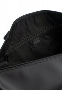 Interno di una borsa in tessuto nero con una superficie liscia, caratterizzato da una tasca con zip e una piccola etichetta nera che mostra "HEXAGONA."