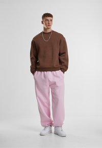 Sudadera marrón de corte holgado, combinada con pantalones de chándal rosas, con cintura elástica y bolsillos, complementada con zapatillas blancas.