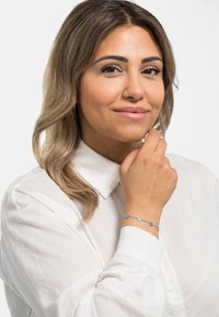 Bracciale d'argento con accenti circolari, indossato su un polso; la persona indossa una camicia bianca con colletto in un tessuto textured.