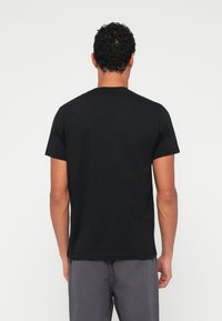 Melna īsām piedurknēm t-kreklā izgatavots no gludas auduma ar klasisku apaļu kakla izgriezumu, redzams no aizmugures bez redzamām rakstu vai logotipa.