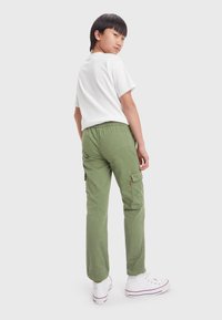 Pantaloni cargo verdi in cotone, con tasche laterali e cintura elasticizzata. Abbinati a una t-shirt bianca a maniche corte e sneakers bianche.