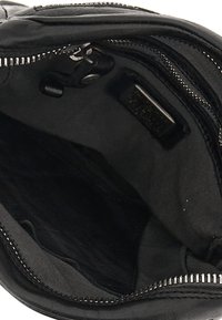 Interno di una borsa in pelle nera con texture liscia, chiusura con zip e più scomparti. Foderata con tessuto nero. Hardware in metallo visibile.