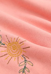 Tessuto rosa con ricamo di sole dal disegno a spirale in giallo e foglie verdi. Texture liscia con dettagli di cucitura visibili.