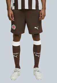 Brune fodboldshorts med hvide striber, med et "FC St. Pauli" logo. Hvid Puma-logo på shortsene og mørkebrune sokker med hvide accenter.