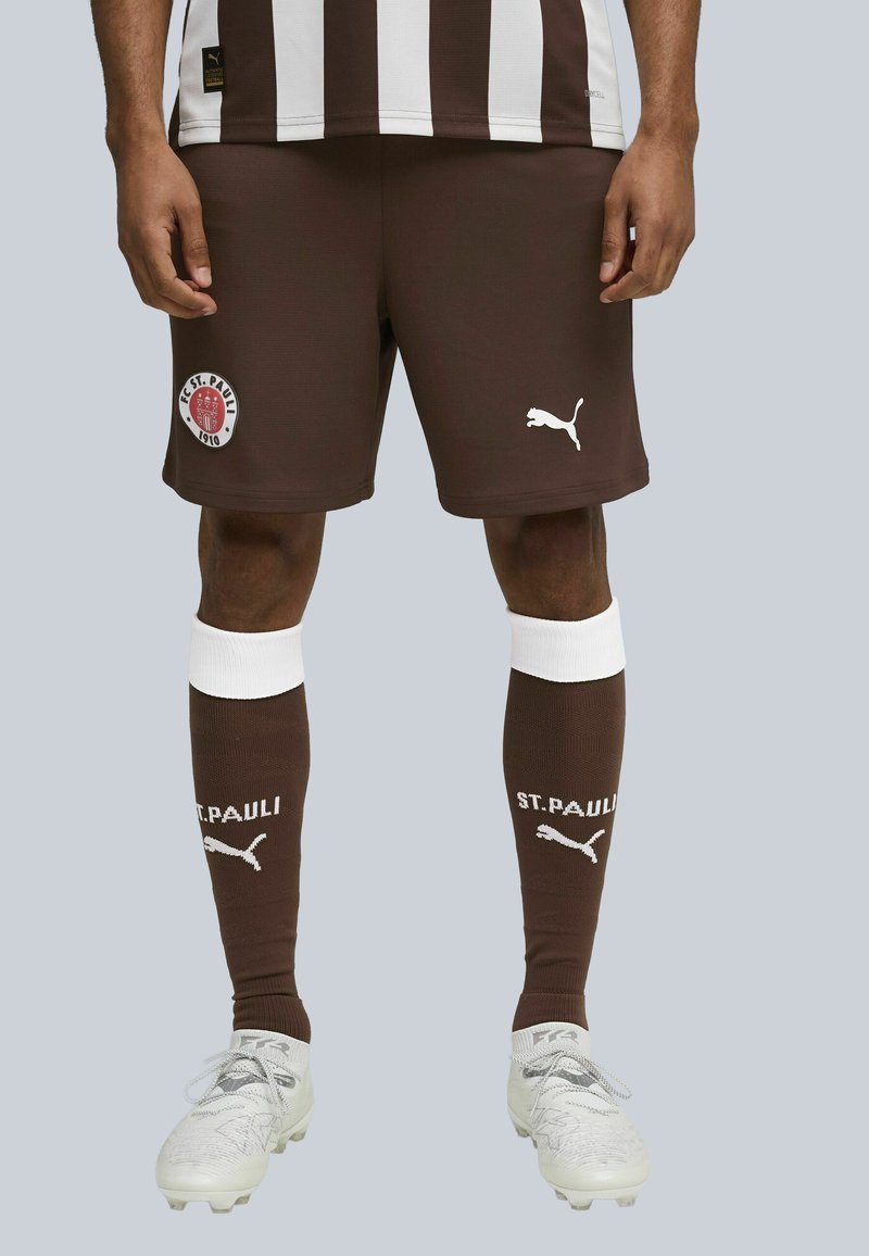 Pruunid jalgpallishortsid valgete triipudega, millel on "FC St. Pauli" logo. Valge Puma logo lühikeste pükste peal ja tumepruunid sokid valgete aktsentidega.