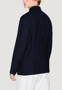 Giacca tailored blu navy con un design elegante, colletto a punte e vestibilità strutturata. Presenta un tessuto liscio e dettagli di cucitura minimalisti.