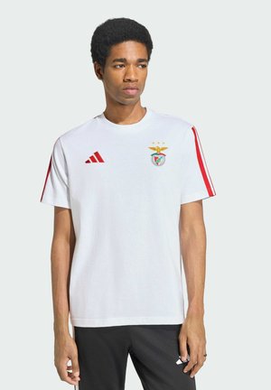 Joven con camiseta deportiva blanca con el logo rojo de Adidas y el emblema del club de fútbol Benfica, mirando hacia su izquierda.
