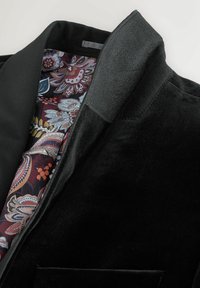 Sort fløjlsblazer med sjalkrave; indersiden har et farverigt blomsterprintfor i burgunderrød, blå og creme.