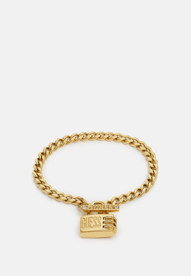 Bracelet chaîne en or avec un pendentif cadenas rectangulaire gravé "GUESS" et orné de petits cristaux clairs.