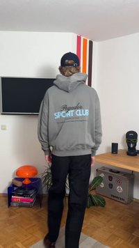 Sweatshirt cinzento com capuz com a inscrição "Pegador Sport Club" em letras azul claro nas costas, combinado com calças pretas. Design casual, corte descontraído.