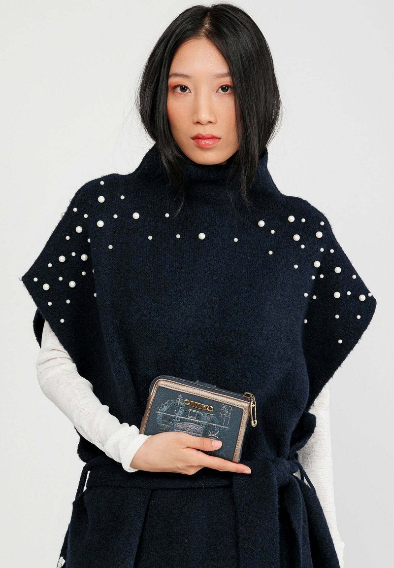 Poncho knit blu navy con colletto alto, impreziosito da perle bianche. Abbinato a un portafoglio blu scuro con chiusura a zip e design grafico.