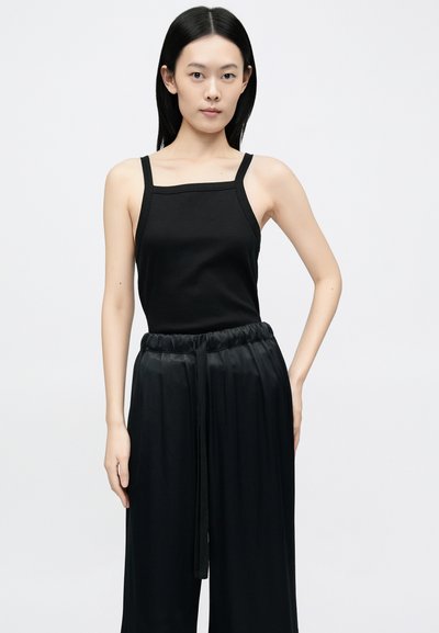 Crni rebrasti top bez rukava kvadratnog izreza i tankih naramenica, uparen s visokim strukom, širokim crnim hlačama koje imaju vezicu u struku.