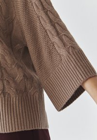 Brauner Strickpullover mit Zopfmuster, gerippten Bündchen und strukturiertem Stich. Lockere Passform mit weiten Ärmeln und weichem Stoff.