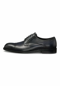 Scarpe eleganti in pelle nera con una finitura liscia, punta rotonda, sei occhielli e una suola nera bassa e piatta. Branding discreto vicino al tallone.