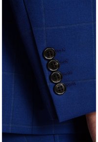 Rękaw niebieskiej marynarki z czterema czarnymi guzikami, wykonany z fakturowanej tkaniny i z widocznymi detalami ściegów.