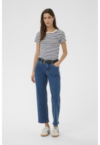 Camiseta de rayas de manga corta en azul marino y crema; jeans ajustados de cintura alta en azul; cinturón negro; zapatillas blancas. La modelo está de pie con las manos en los bolsillos.