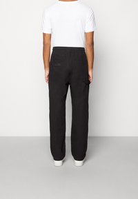 Svarta byxor med avslappnad passform, elastisk midja och två bakfickor. Materialet verkar mjukt, med en slät yta och minimal detaljering.