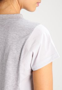 Szaro-biała koszulka z krótkim rękawem o gładkiej fakturze, z raglanowym krojem oraz kontrastującymi kolorami na ramionach.